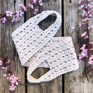 May include: A white crocheted bag with a unique design. The bag has two straps and a wide opening. The bag is lying on a wooden surface.