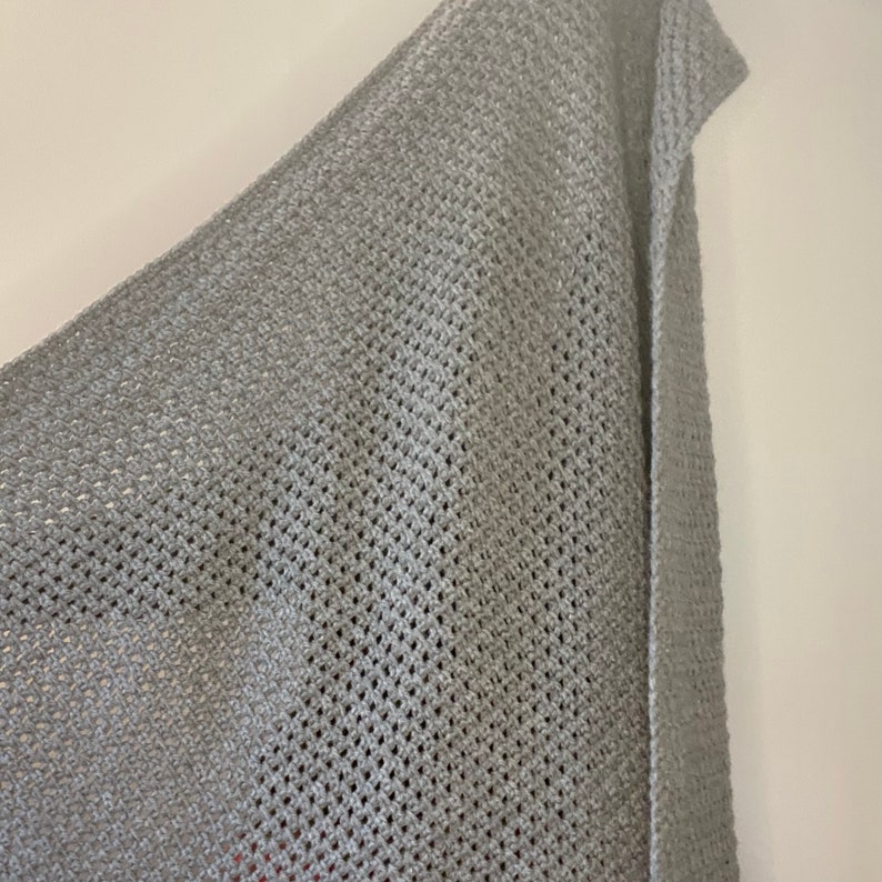 K&ouml;nnte beinhalten: Nahaufnahme eines grauen gestrickten Stoffes mit einem Netz-Muster. Der Stoff hat einen dezenten Glanz und eine weiche Textur.
