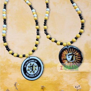 May include: Two necklaces with black, white, and yellow beads. One necklace has a pendant with the text "In the name of the gods & earths" and a seven-pointed star. The other necklace has a pendant with a sun, moon, and seven-pointed star.