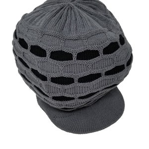 May include: A gray knit hat with a visor. The hat features a unique design with openwork sections revealing a black interior. The hat is made of a soft, textured material and is suitable for casual wear.