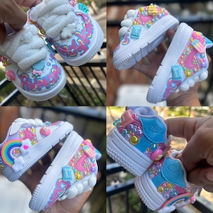 May include: A pair of white sneakers with a candy theme. The sneakers are decorated with colorful sprinkles, candies, and a rainbow. The text "Sweet" is written on the side of the sneakers.