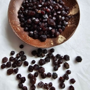 Puede incluir: Un cuenco de madera lleno de cristales de granate rojo oscuro. Algunos cristales están dispersos sobre una superficie blanca.