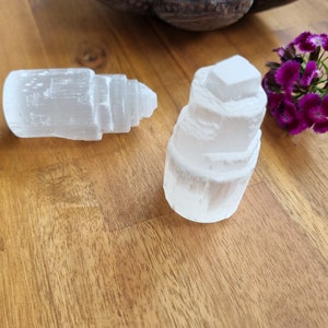 May include: Two white selenite crystal towers, one stacked higher than the other, on a wooden surface.