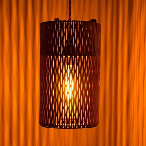 Puede incluir: Una lámpara colgante con una pantalla de madera, geométrica y en forma de jaula. La luz está encendida y proyecta un brillo cálido.