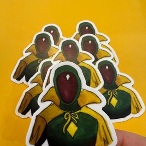 Pu&ograve; includere: Un set di otto adesivi con un personaggio verde e giallo con un diamante sul petto. Il personaggio ha un viso rosso con cappuccio e un mantello giallo.
