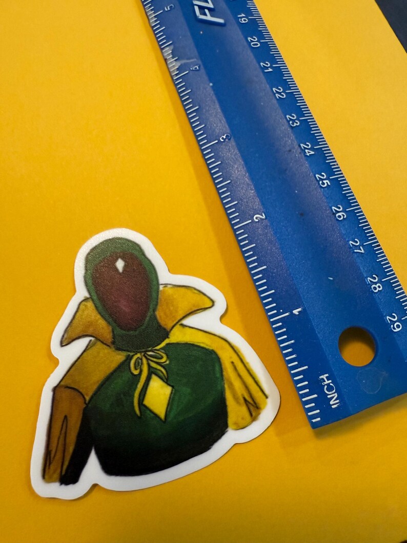 Pu&ograve; includere: Un adesivo verde e giallo di un personaggio che indossa un mantello con cappuccio e un diamante sul petto.