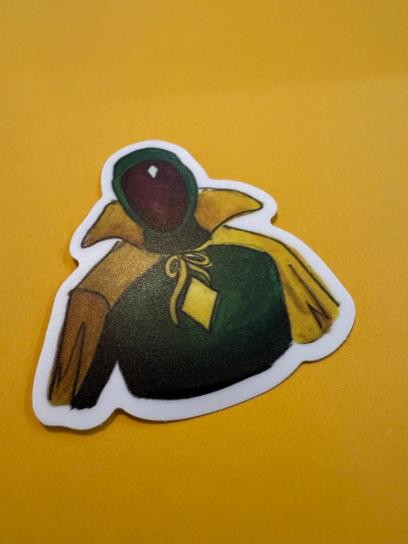 Pu&ograve; includere: Un adesivo con un'illustrazione di un personaggio dei cartoni animati che indossa una tunica verde con cappuccio, un colletto giallo e un diamante giallo sul petto.