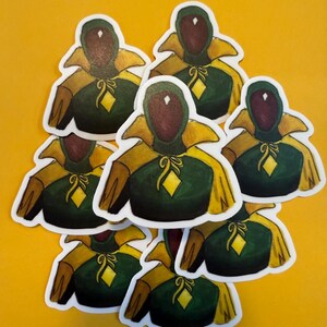 Pu&ograve; includere: Otto adesivi verdi e dorati con un personaggio dei cartoni animati con un diamante sulla fronte. Il personaggio indossa una tunica verde e dorata con un colletto giallo e una fascia gialla.