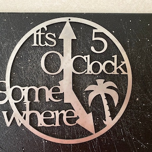Puede incluir: Un letrero de metal con el texto "It's 5 O'Clock Somewhere" y un gráfico de palmera.