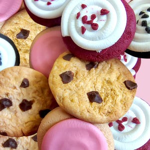 May include: An assortment of colorful cookies and cupcakes. The image features chocolate chip cookies, pink frosted cookies, and cupcakes with white frosting and red sprinkles. The treats are arranged on a pink background.