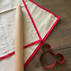Pastry Cloth spread out on a wooden table with a rolling pin on top and a Mickey Mouse shaped cookie cutter next to it.