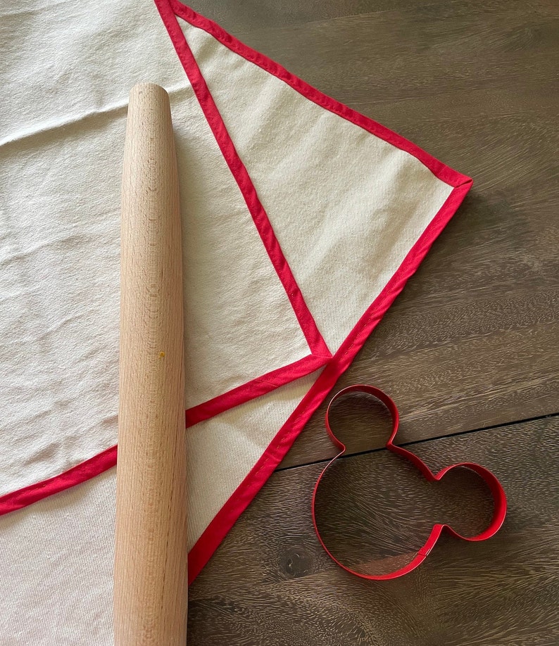 Pastry Cloth spread out on a wooden table with a rolling pin on top and a Mickey Mouse shaped cookie cutter next to it.