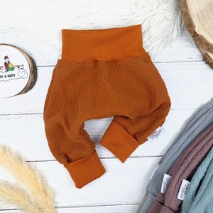 Pu&ograve; includere: Un paio di pantaloni per neonati color ruggine con una cintura pieghevole e gambe con polsini. I pantaloni sono realizzati in un tessuto morbido e testurizzato.