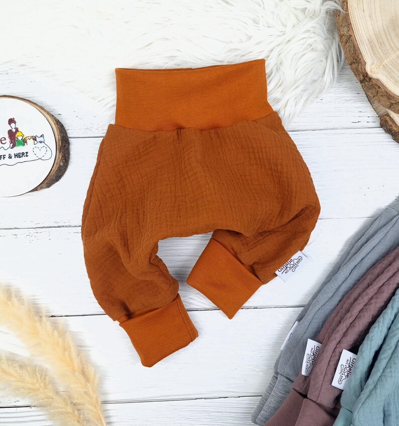 Pu&ograve; includere: Un paio di pantaloni per neonati color ruggine con una cintura pieghevole e gambe con polsini. I pantaloni sono realizzati in un tessuto morbido e testurizzato.