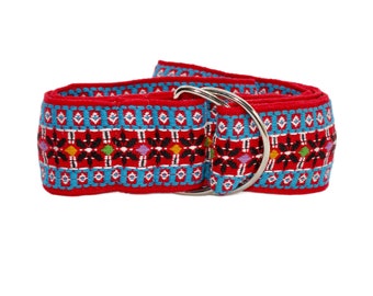 May include: Red belt with a detailed woven pattern in turquoise, black, white, and accents of yellow, green, and purple. The belt features a silver-colored, double-D ring closure. The belt is a fashion accessory.