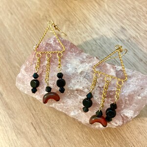 May include: Gold triangle dangle earrings with black beads and a red crescent moon charm.