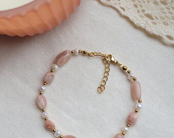 Könnte beinhalten: Ein zartes Armband mit abwechselnden Perlen aus pfirsichfarbenem Sunstone und weißen Perlen. Das Armband hat einen goldfarbenen Kettenverschluss.
