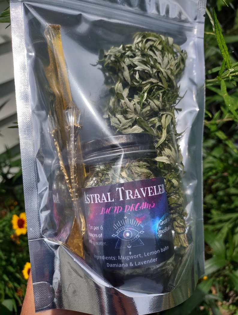 Puede incluir: Una bolsa de pl&aacute;stico transparente que contiene un frasco de vidrio lleno de hierbas secas y un palo de madera. El frasco tiene una etiqueta negra con el texto "Astral Traveler Lucid Dreams" y una lista de ingredientes: Ajenjo, Melisa, Damiana y Lavanda. La etiqueta tambi&eacute;n incluye el texto "1 cucharadita por 170 ml de agua."