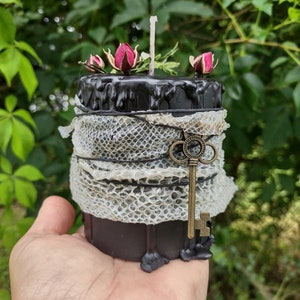 May include: Black candle with a key and dried roses on top. The candle is wrapped in a white snakeskin pattern.