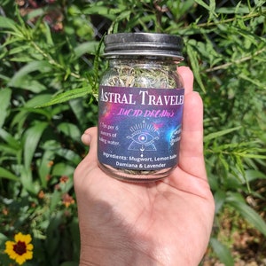 Puede incluir: Un frasco de vidrio lleno de hierbas secas etiquetado como "Astral Traveler Lucid Dreams". La etiqueta tambi&eacute;n incluye el texto "1 cucharadita por 6 onzas de agua hirviendo." e "Ingredientes: Ajenjo, Melisa, Damiana & Lavanda".