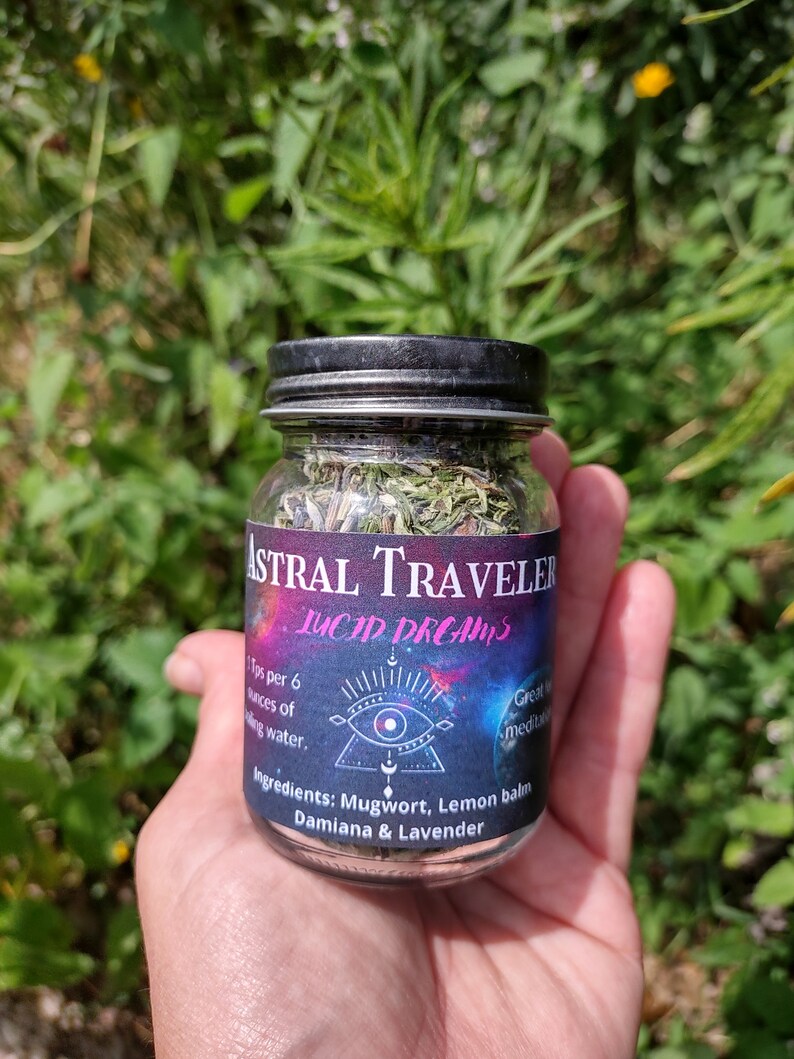 Puede incluir: Un frasco de vidrio con tapa negra lleno de hierbas secas etiquetado como "Astral Traveler Lucid Dreams". La etiqueta tambi&eacute;n incluye el texto "1 cucharadita por 6 onzas de agua. Ingredientes: Ajenjo, Melisa, Damiana & Lavanda. Ideal para la meditaci&oacute;n."
