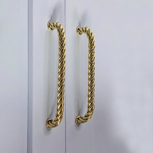 May include: A pair of gold-coloured, twisted rope-style door handles against a white background. The handles are curved and have a polished finish, adding a touch of elegance to the door.