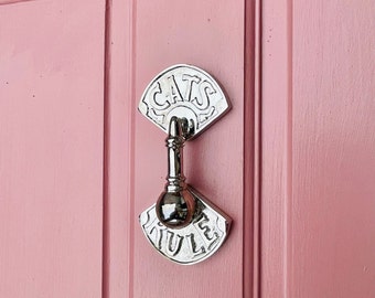 May include: A silver door knocker with the words "Cats Rule" on a pink door.