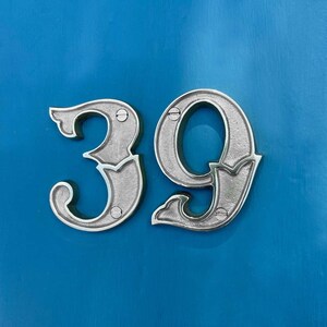 May include: Silver metal house number 39 on a bright blue background.