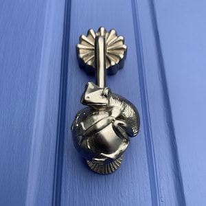 May include: A silver door knocker shaped like a frog holding a sphere. The knocker is mounted on a blue door.
