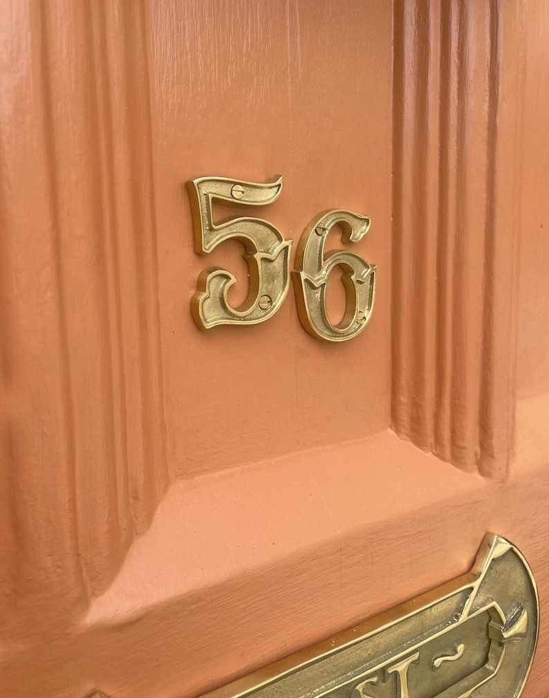 May include: A close-up of a peach-colored door with a brass house number "56" attached. The number is in a decorative, ornate font.
