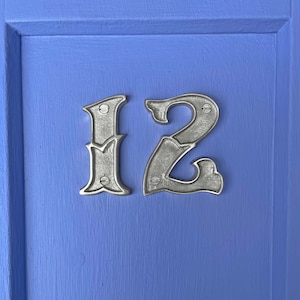 May include: A close-up of a silver house number plaque with the number "12" on a blue door.