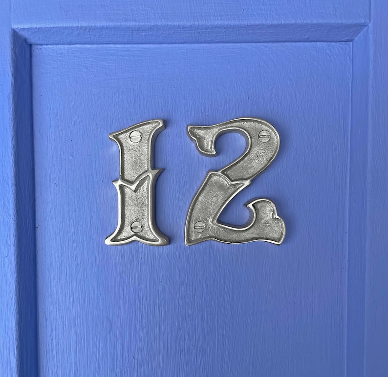 May include: A close-up of a silver house number plaque with the number "12" on a blue door.