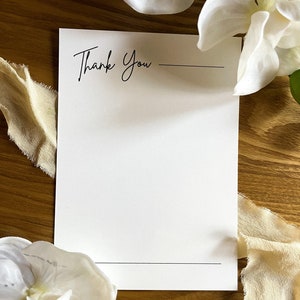 May include: A white card with the text "Thank You" written in black cursive. There is a line under the text and another line at the bottom of the card.