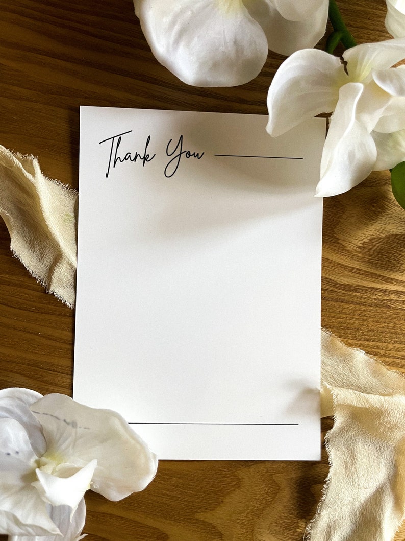 May include: A white card with the text "Thank You" written in black cursive. There is a line under the text and another line at the bottom of the card.