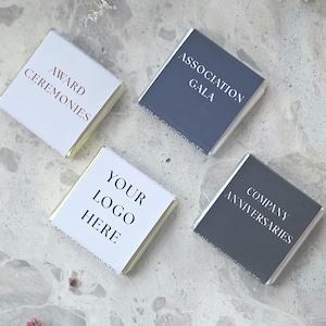 May include: Four individually wrapped chocolate bars with text. The bars have white and dark blue wrappers. Text on the wrappers includes "Award Ceremonies", "Association Gala", "Your Logo Here", and "Company Anniversaries".