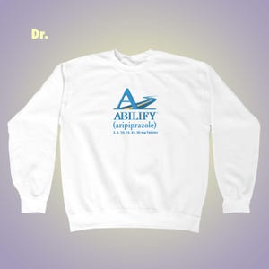 May include: White sweatshirt with the word "ABILIFY" in blue and yellow, along with the chemical name aripiprazole and tablet dosages. The letter "A" is stylized with a road design. The word "Dr." is in the upper left corner.