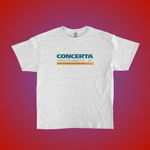 Peut inclure: T-shirt gris clair avec le mot "CONCERTA" en turquoise, et "methylphenidate HCI" en dessous. Le t-shirt affiche également des informations sur le dosage dans une barre orange. Le design est centré sur le t-shirt.