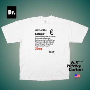 May include: A white short-sleeve t-shirt featuring a black graphic print of a prescription label for Adderall 20 mg. The text includes NDC 57844-120-01, chemical ingredients, and Rx only. The shirt is made of 6.5 oz/yd² heavy cotton fabric.