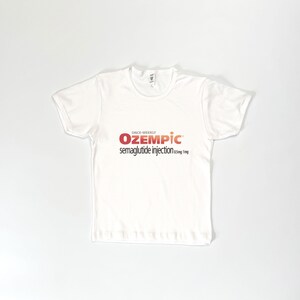 May include: White t-shirt with the text "OZEMPIC" in red and orange, with the words "semaglutide injection 0.5mg 1mg" below. The shirt is short-sleeved and made of a soft material.