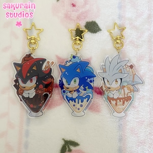 Op de afbeelding: Drie acryl sleutelhangers met personages uit Sonic the Hedgehog. Elke sleutelhanger toont een personage in een ijscoupe met gouden stervormige sluitingen. De personages zijn Shadow, Sonic en Silver.