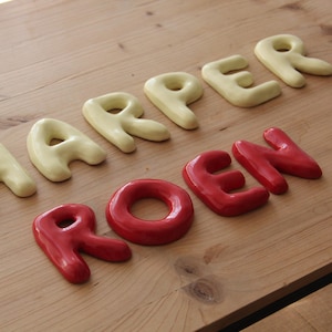 May include: Wooden table with the names "HARPER" and "ROEN" spelled out in individual, three-dimensional letters. The letters for "HARPER" are a pale yellow, while "ROEN" is in red.