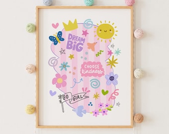 May include: A framed art print with a light wood frame. The artwork features a pink and white striped background with various colorful illustrations, including a butterfly, sun, flowers, and the phrases "Dream Big" and "Choose Kindness."