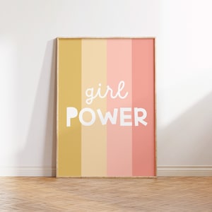 May include: A framed print with a striped background in shades of yellow, cream, and pink. The text "girl power" is written in white on the print.