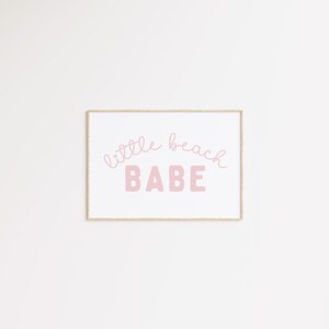 May include: A framed print with the text "little beach BABE" in pink lettering on a white background.