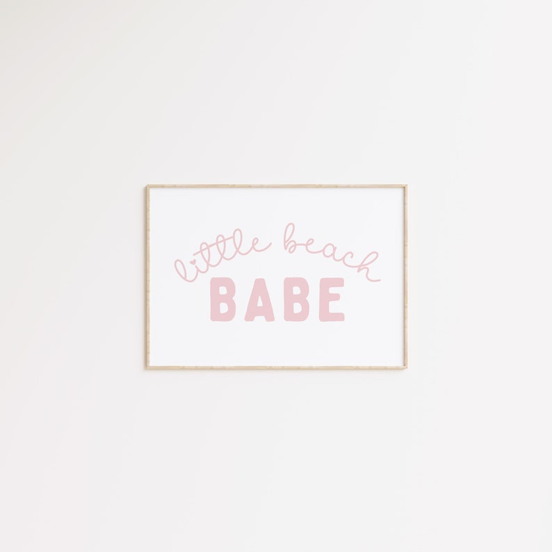 May include: A framed print with the text "little beach BABE" in pink lettering on a white background.