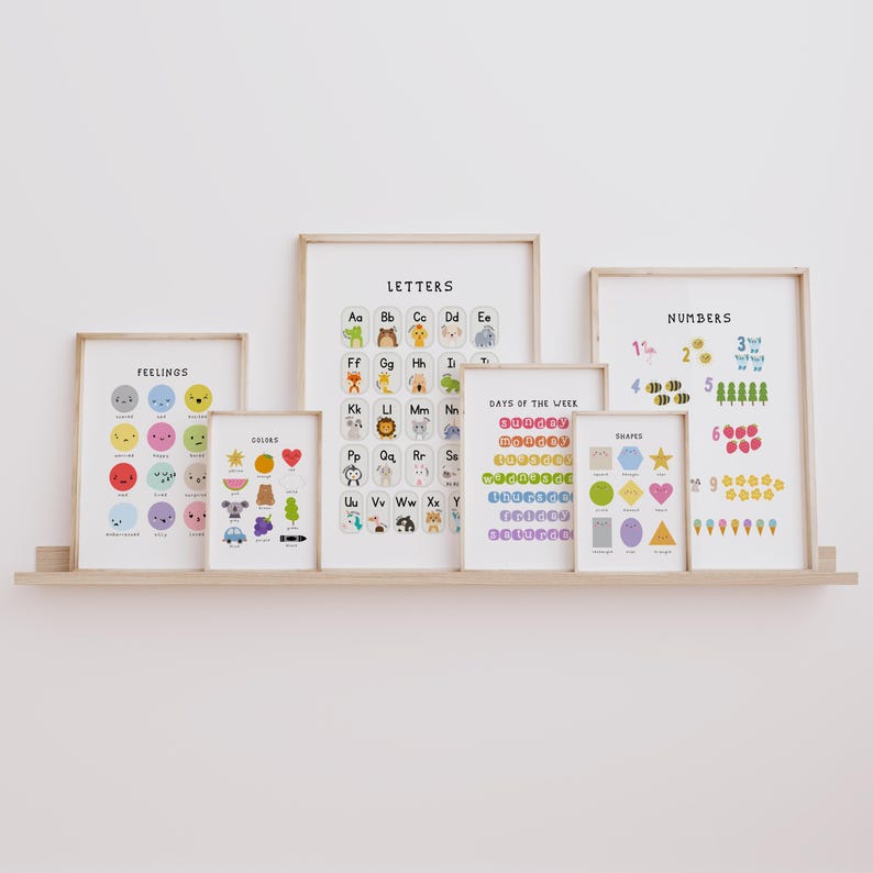 May include: A collection of framed educational posters displayed on a wooden shelf. The posters feature colorful illustrations of letters, numbers, shapes, colors, days of the week, and feelings. The frames are a light wood color.