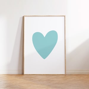 Op de afbeelding: Een ingelijste kunstdruk met een groot, effen turquoise hart op een witte achtergrond. Het kunstwerk wordt gepresenteerd in een lichtgekleurde houten lijst, leunend tegen een witte muur. De vloer is gemaakt van lichtgekleurde houten planken.