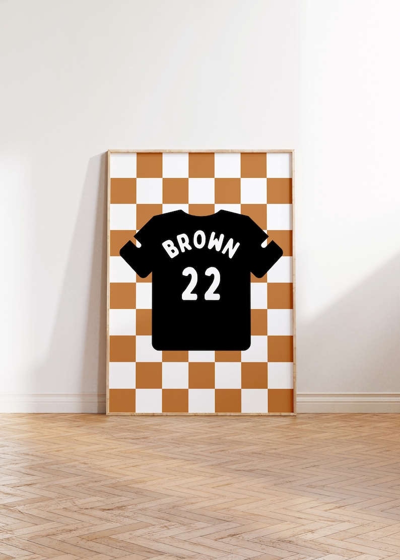 Op de afbeelding: Een ingelijst print met een zwart-wit geruit patroon. Een zwart shirt met het woord "BROWN" en het nummer "22" in wit is gecentreerd op het geruite patroon.
