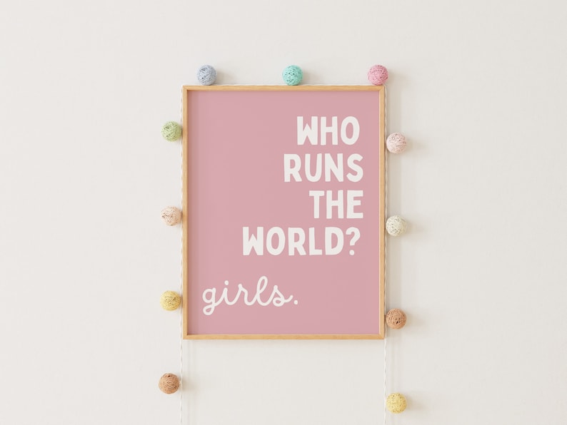 May include: A pink framed print with the text "Who runs the world? girls."  The print is surrounded by a string of colorful pom-poms.