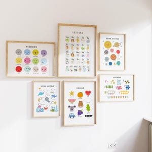 May include: A collection of framed educational posters on a white wall. The posters feature colorful illustrations of feelings, letters, ocean animals, colors, the solar system, and numbers. Each poster has a wooden frame.